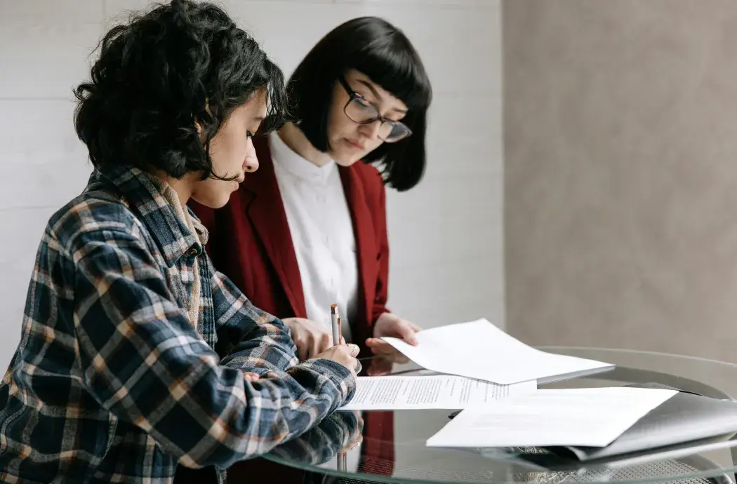 テーブルの上に置かれた書類を見ながら話す2人の女性。